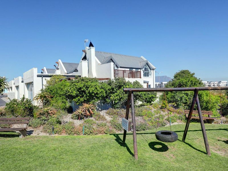 A view of the rear elevation of the townhouse, featuring a landscaped garden, balcony, and well-maintained exterior finishes.