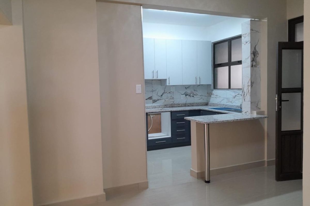 A compact kitchen featuring modern two-tone cabinetry, granite countertops, a breakfast bar, and a marble-look backsplash, currently awaiting appliance installation.