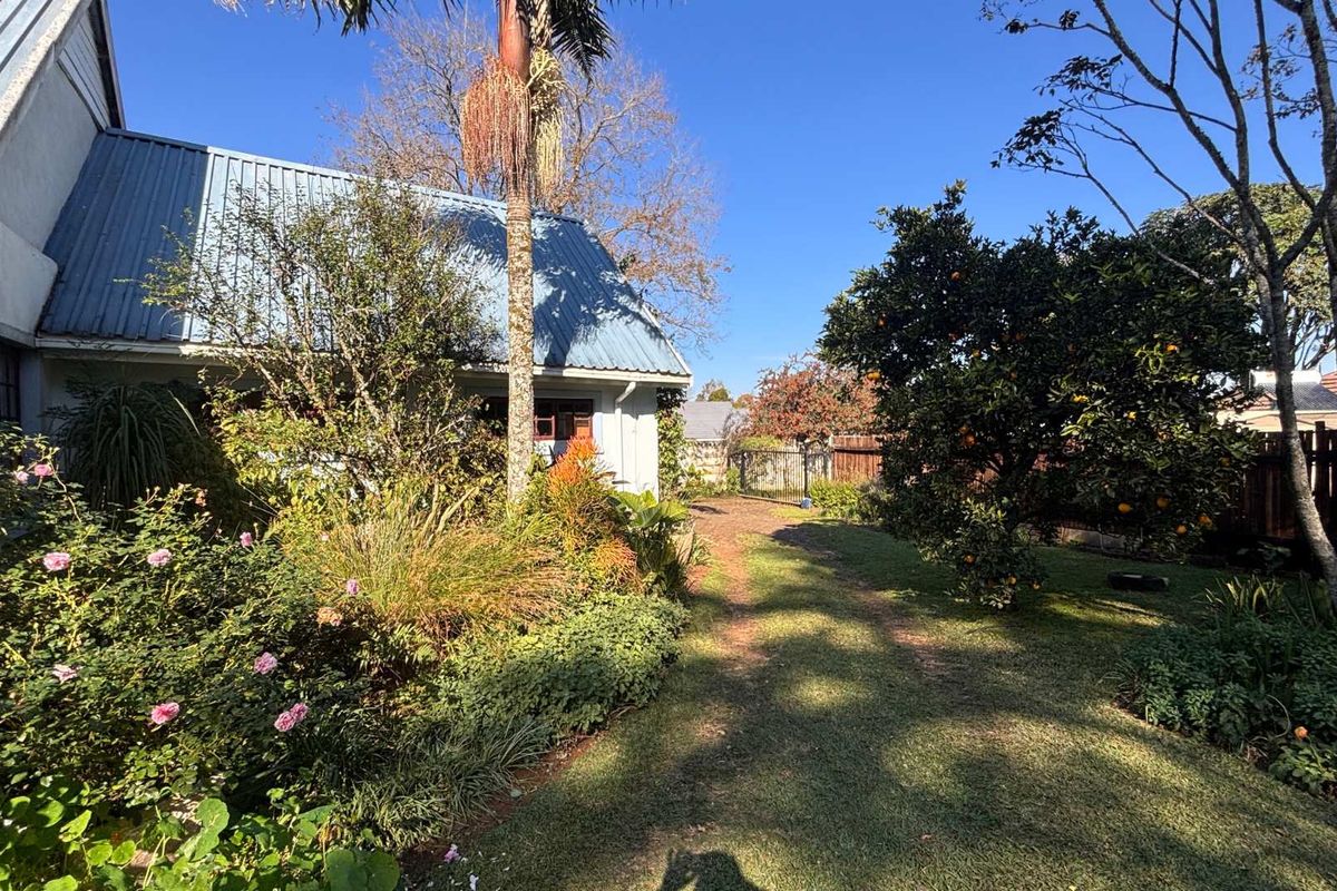 A view of the rear garden featuring established landscaping, mature trees, and a clear view of the house's exterior facade and metal roof.
