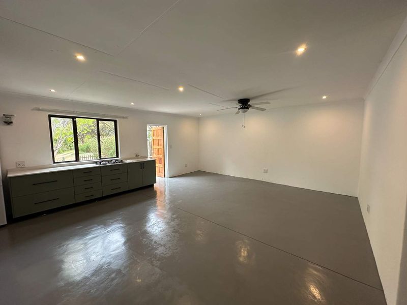 Spacious open-plan living area featuring a modern kitchen with built-in cabinetry, gas hob, and polished concrete flooring, offering a clean and versatile layout.