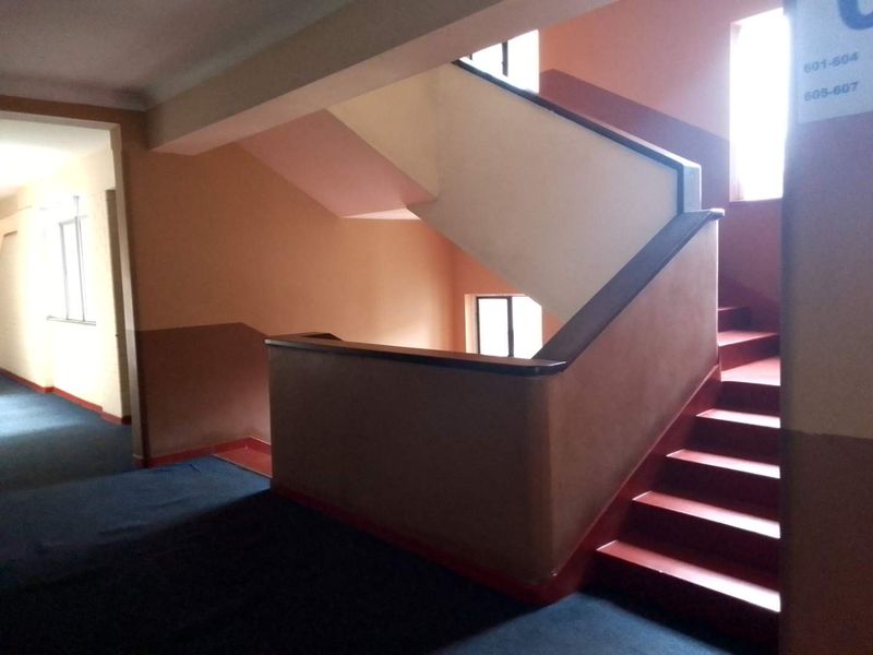 A communal apartment building hallway featuring a staircase with a handrail and directional signage.