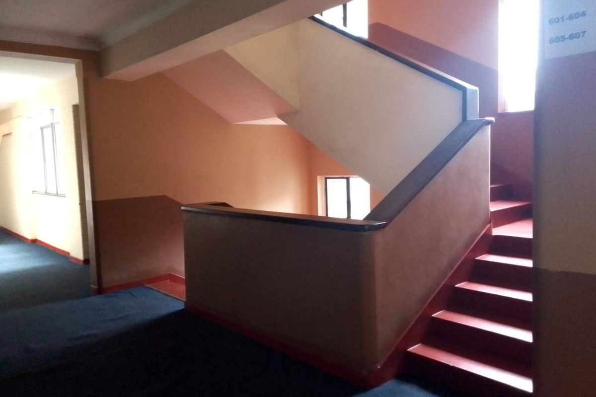 A communal apartment building hallway featuring a staircase with a handrail and directional signage.