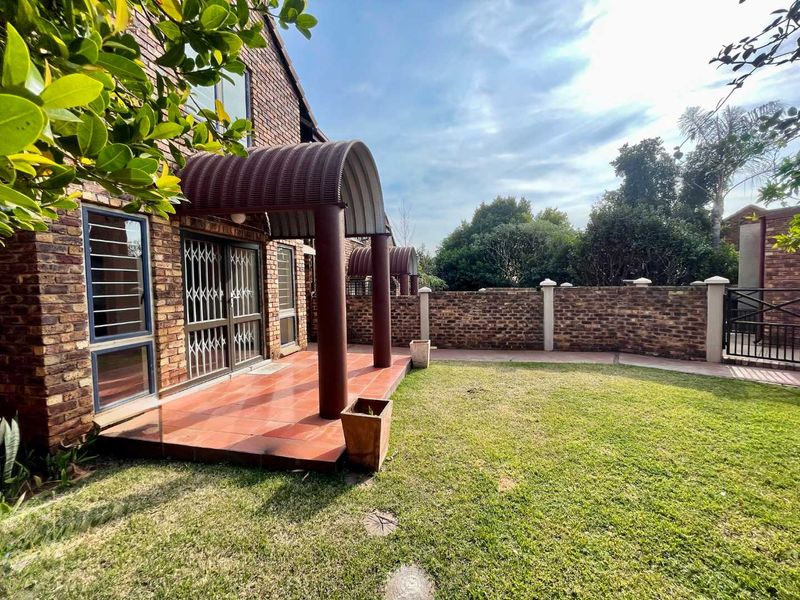 Rear view of the townhouse featuring a face brick facade, a covered tiled patio with a curved awning, and a private garden area.