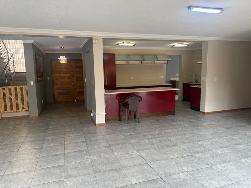 Spacious open-plan living area featuring tiled floors, a central kitchen island with stone countertops, and a grand wooden entrance door.