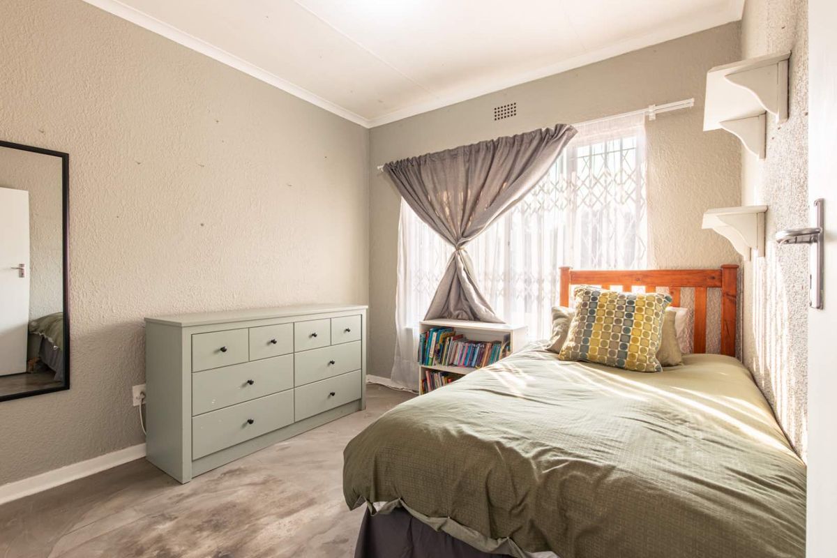 A functional bedroom featuring textured walls, a window with security gate, and built-in wall shelving.
