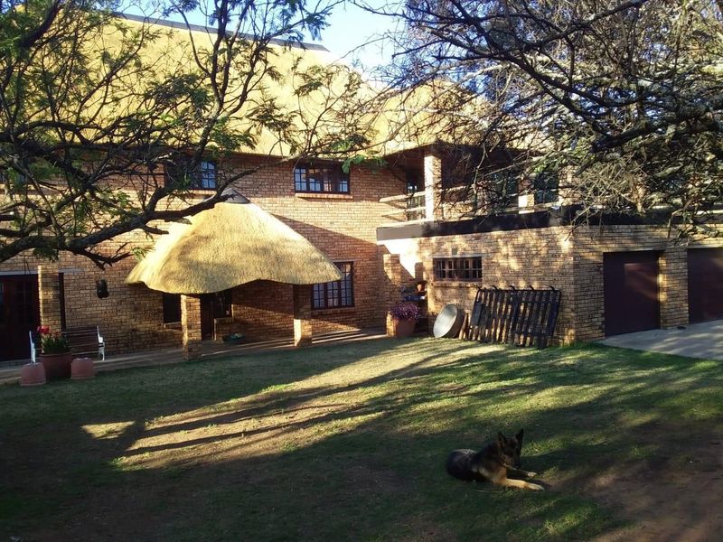 Rear view of a two-story face brick farmhouse featuring a thatched roof, covered patio area, and attached garage set within a spacious garden.