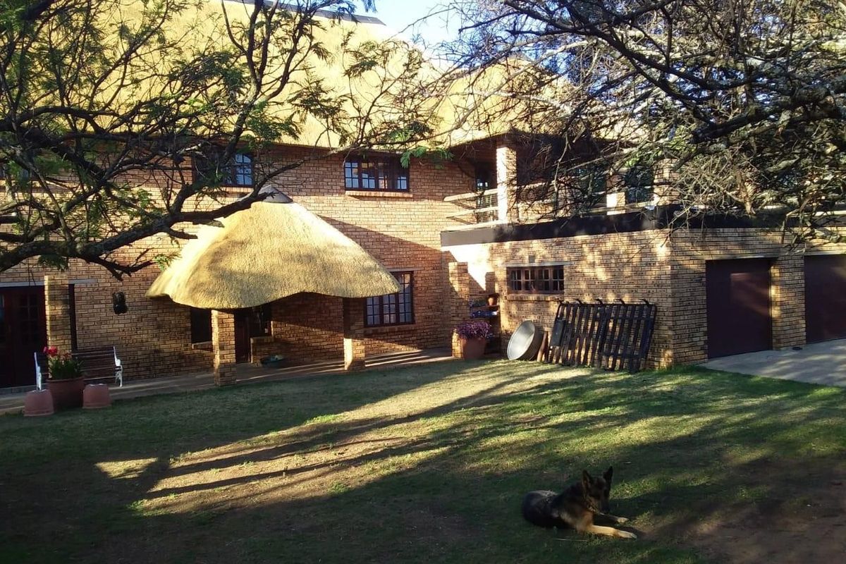 Rear view of a two-story face brick farmhouse featuring a thatched roof, covered patio area, and attached garage set within a spacious garden.