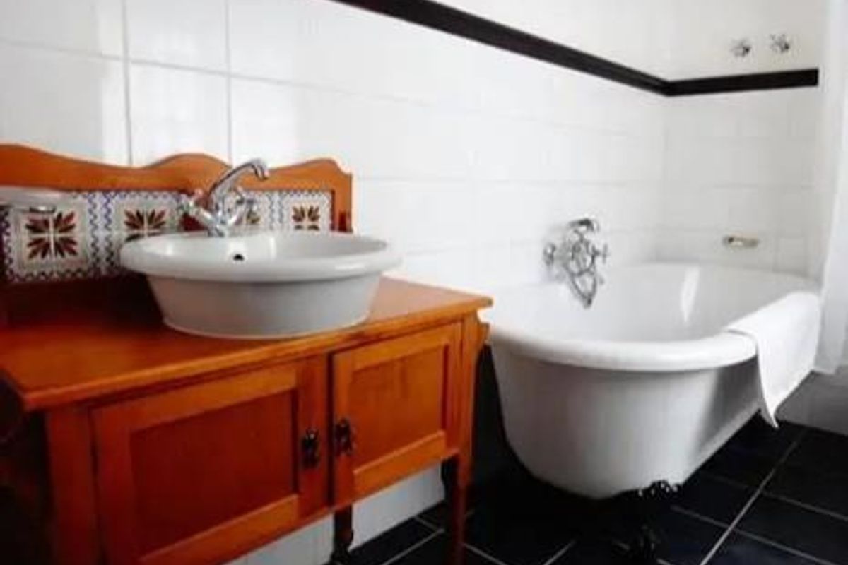 A classic bathroom featuring a clawfoot bathtub, a vessel sink set on a wooden vanity, and white wall tiling with black accent trim.
