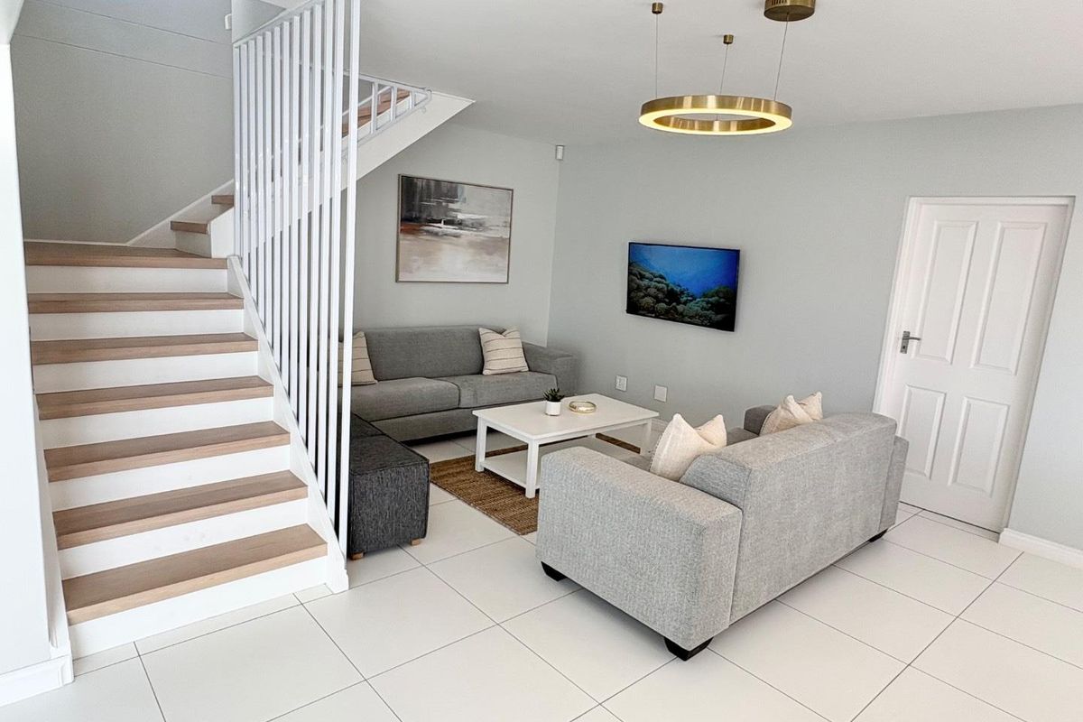 Bright and modern living room featuring tiled flooring, a contemporary staircase with white balustrades, and a stylish circular pendant light fixture.