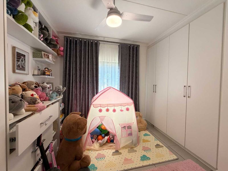 A well-maintained bedroom featuring extensive built-in cupboards, integrated shelving, and a ceiling fan, providing ample storage and comfortable climate control.