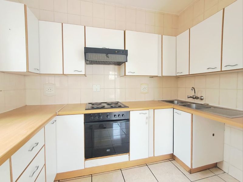 A functional kitchen featuring white cabinetry, laminate countertops, a built-in oven, electric hob, and a double basin sink with tiled splashbacks.
