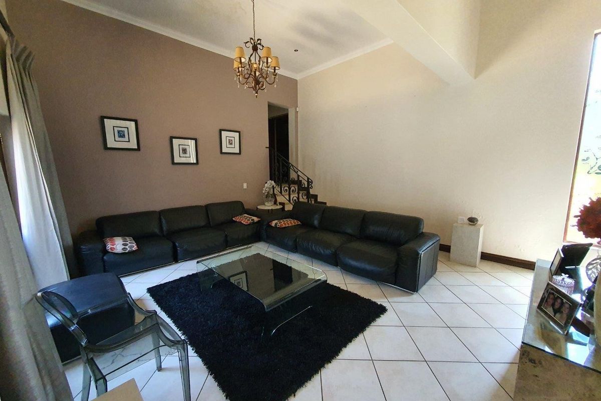 Spacious living room featuring high vaulted ceilings, tiled flooring, and an elegant wrought iron staircase leading to the upper level.
