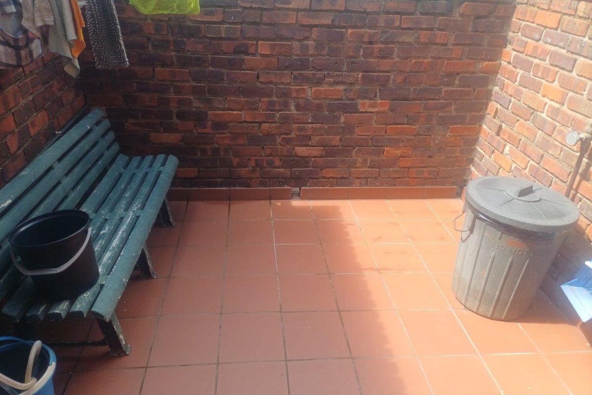 A private outdoor courtyard area featuring exposed brick walls and tiled flooring, suitable for a small utility or relaxation space.