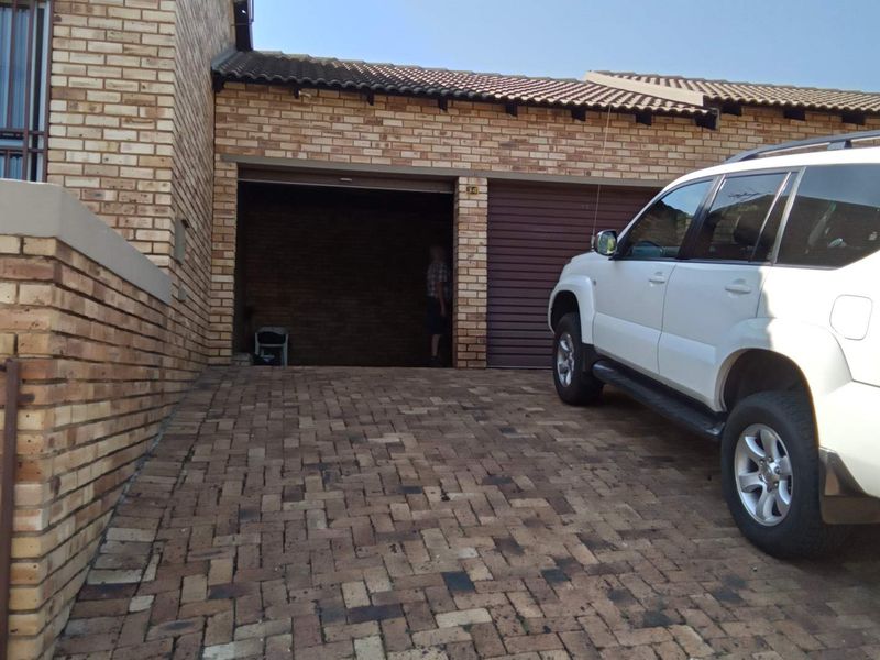 Front exterior view of a townhouse featuring a brick facade, tiled roof, and a paved driveway leading to a double garage.