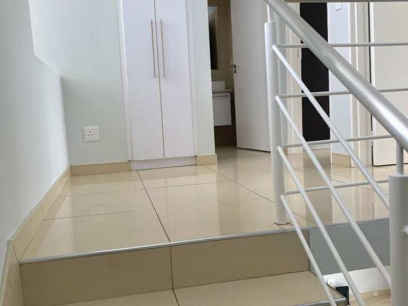 A bright, modern hallway featuring a tiled staircase with a sleek metal balustrade and a built-in storage cupboard.