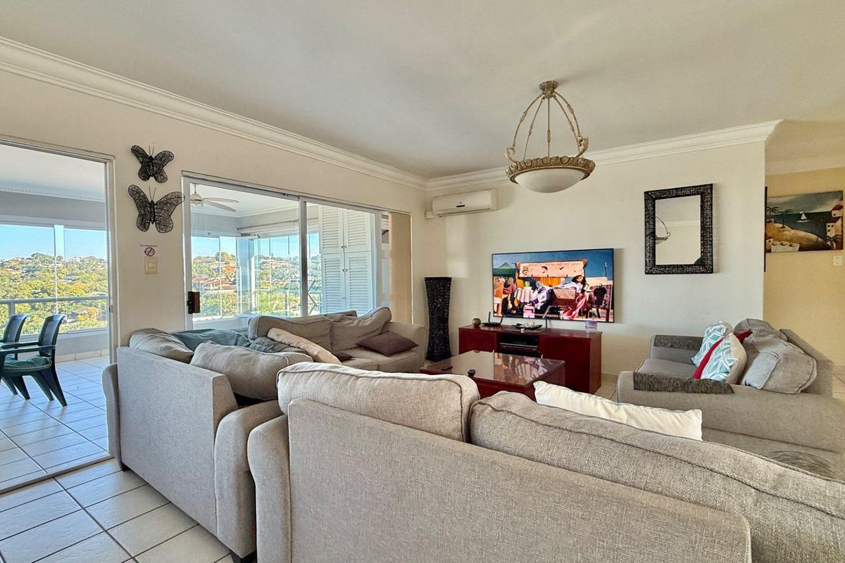 Spacious living room featuring tiled flooring, crown molding, a wall-mounted air conditioning unit, and large sliding glass doors leading to an enclosed balcony.