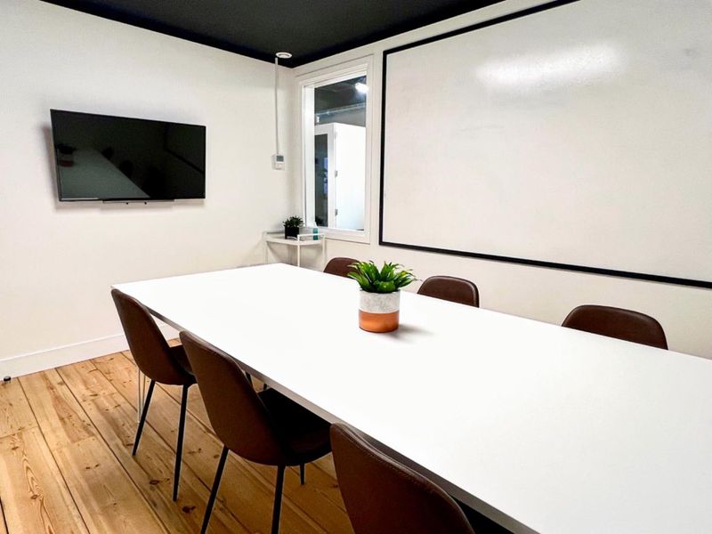 A modern office meeting room featuring hardwood flooring, a large wall-mounted whiteboard, and a clean, minimalist aesthetic suitable for professional collaboration.