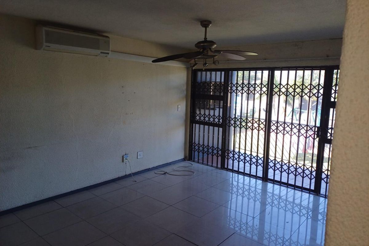 An empty living room featuring tiled flooring, a ceiling fan, a wall-mounted air conditioner, and a security gate leading to an outdoor area.