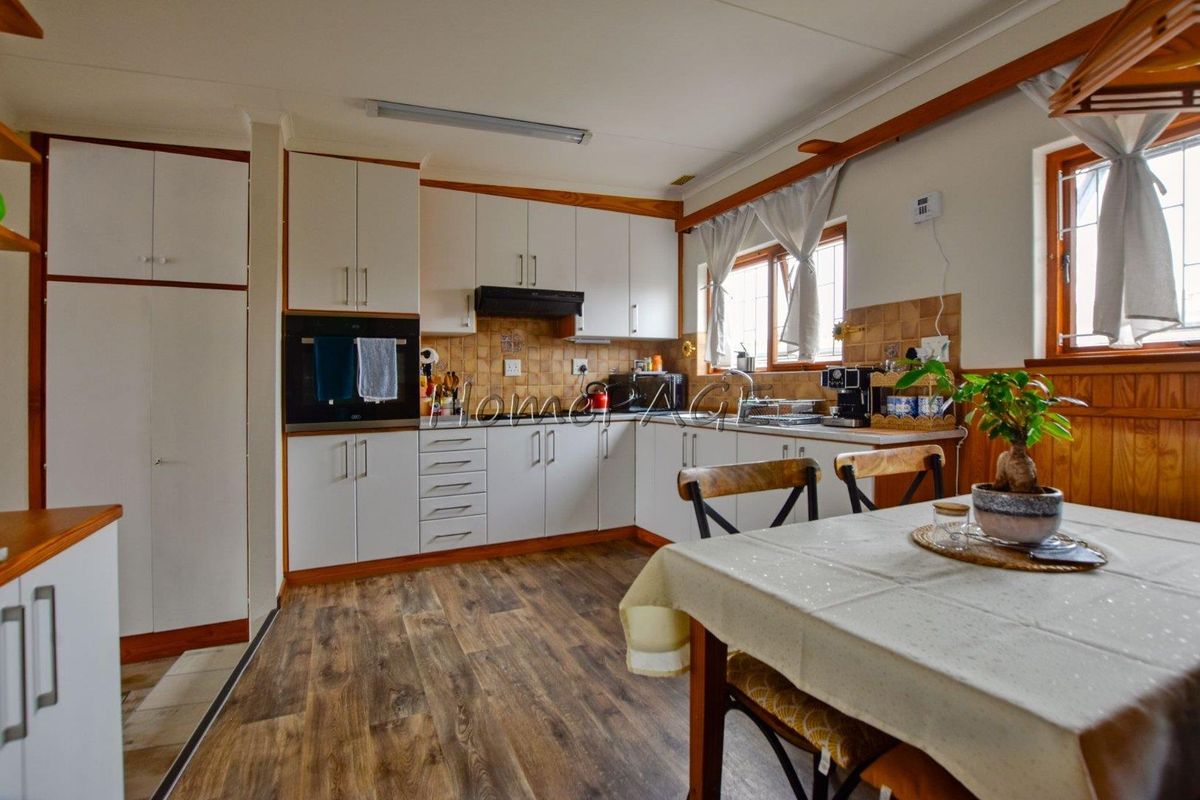 A functional kitchen featuring white cabinetry, wood-look laminate flooring, tiled backsplash, and integrated appliances, offering a practical layout for daily meal preparation.