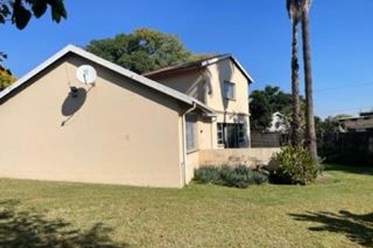 Rear view of the two-story house featuring a lawn, garden area, and exterior wall with a satellite dish.