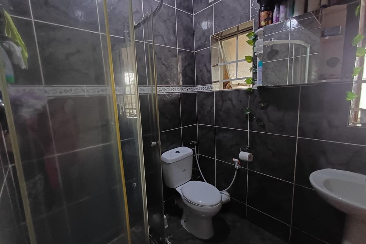 A compact bathroom featuring dark marble-effect wall tiles, a glass shower enclosure, a pedestal basin, and a standard toilet with a bidet spray.