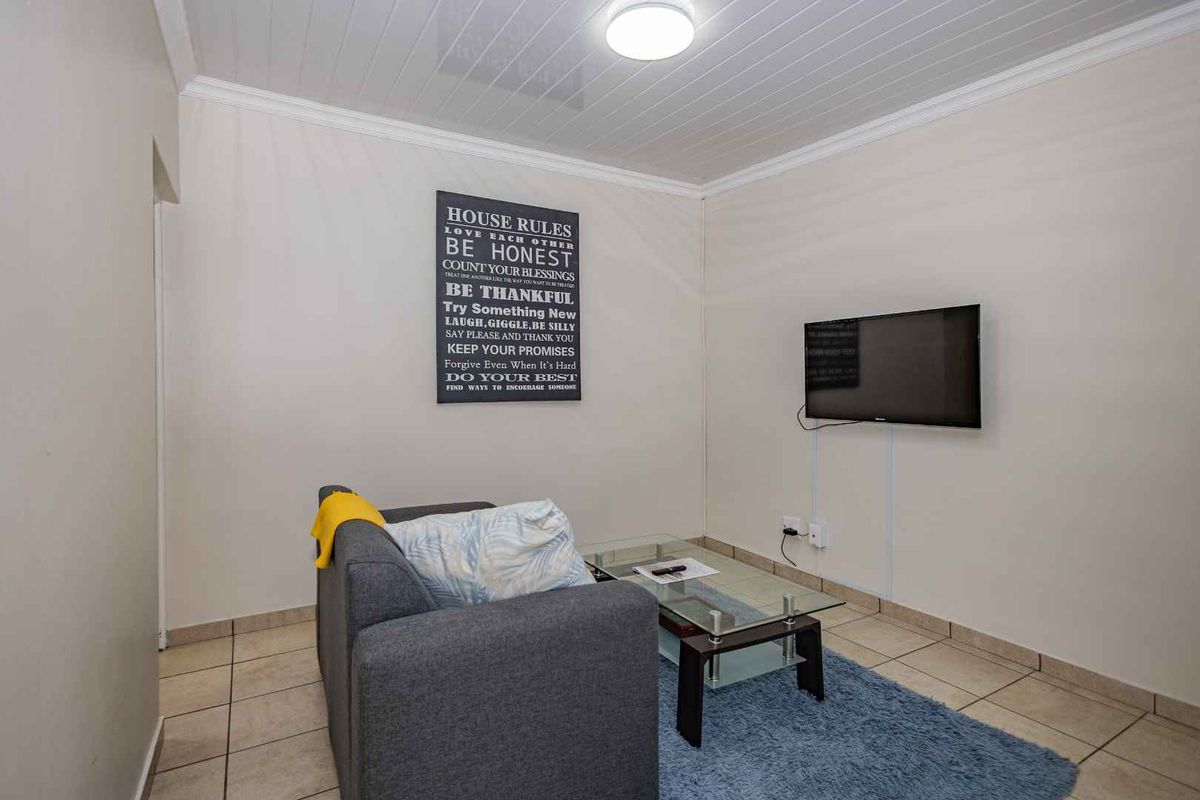 A living room featuring tiled flooring, a tongue-and-groove ceiling, and a wall-mounted television.