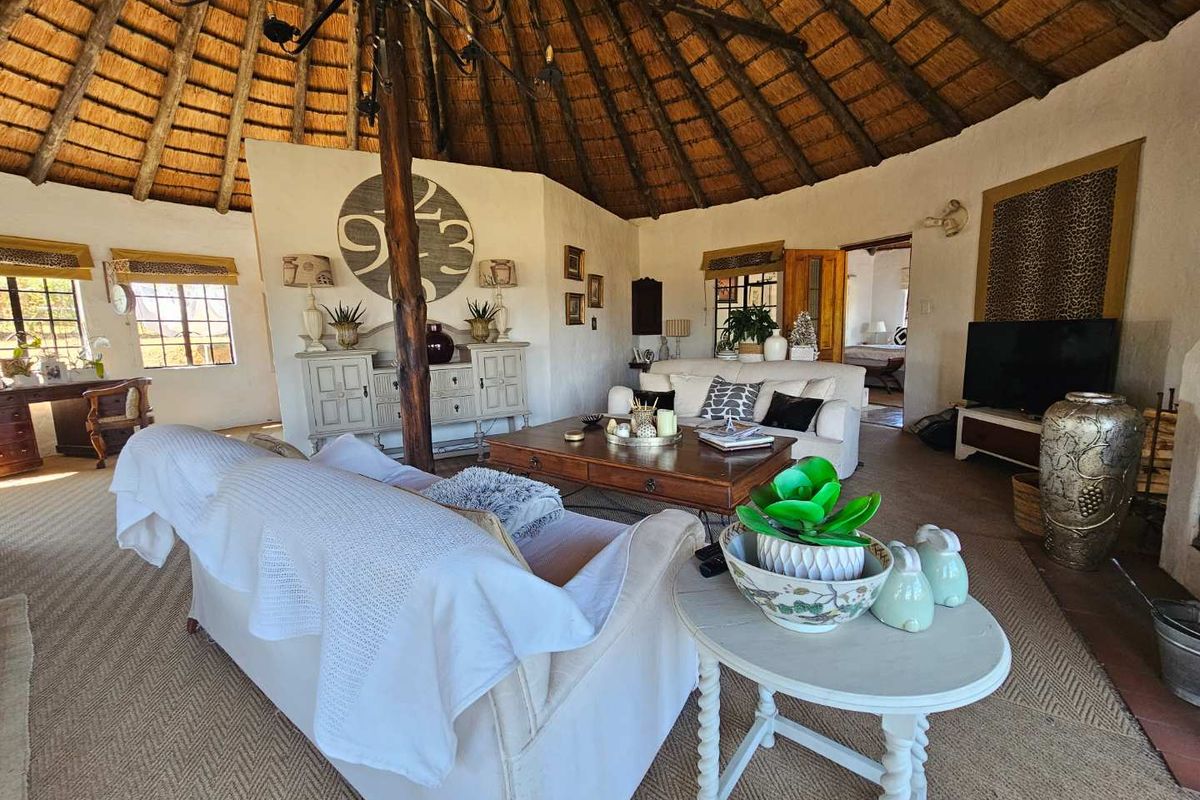 Spacious living room featuring a traditional thatched roof with exposed timber rafters, a fireplace, and tiled flooring in a rustic farm-style setting.