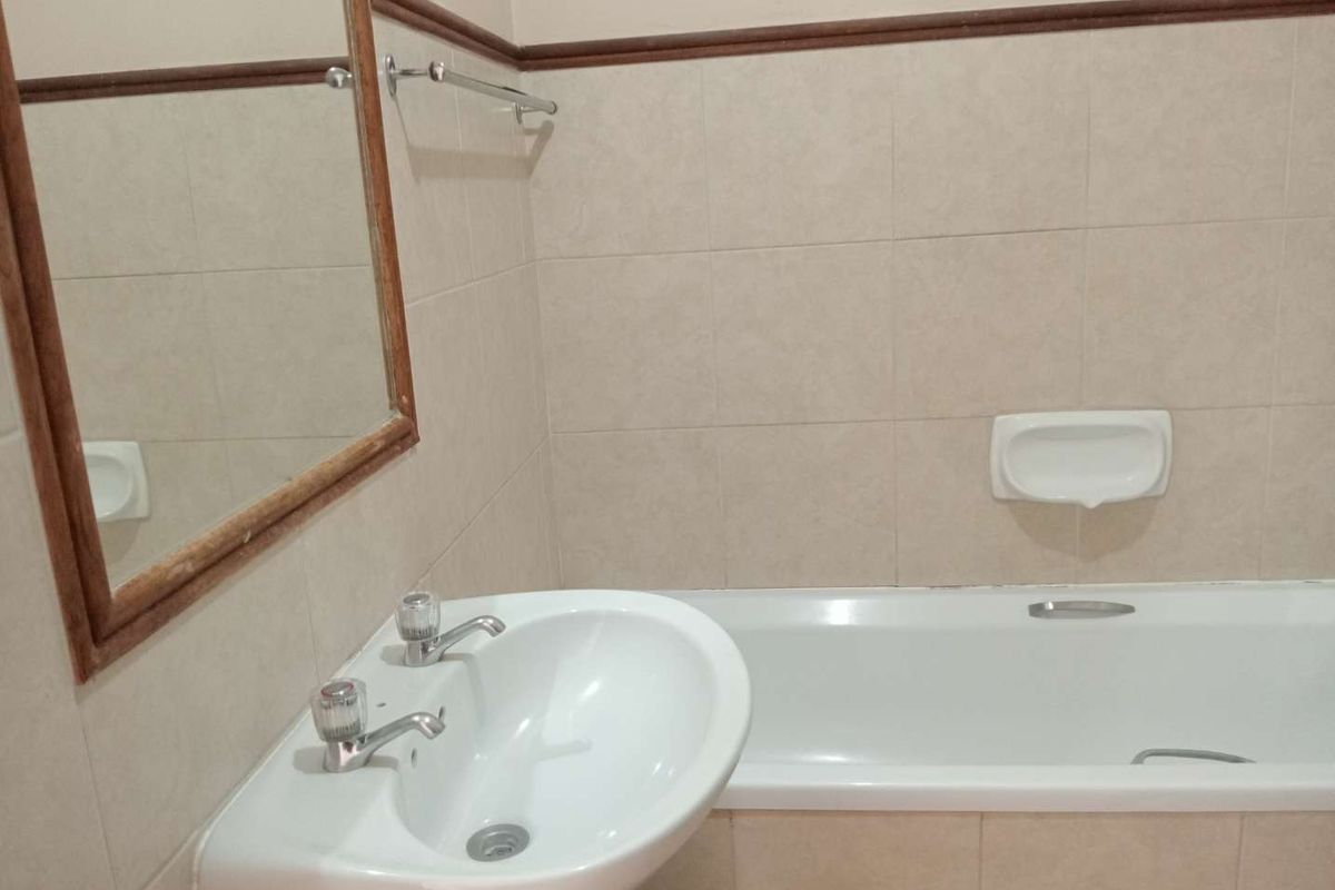 A functional bathroom featuring a pedestal basin, a standard bathtub, and neutral wall tiling, providing a clean and practical space.