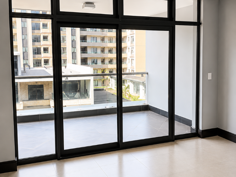 A bright, empty living area featuring large sliding glass doors that open onto a private balcony with modern tiled flooring.
