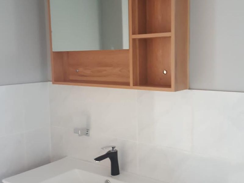 A modern bathroom vanity featuring a wood-finish cabinet, integrated basin with a black mixer tap, and a matching wall-mounted medicine cabinet with open shelving.
