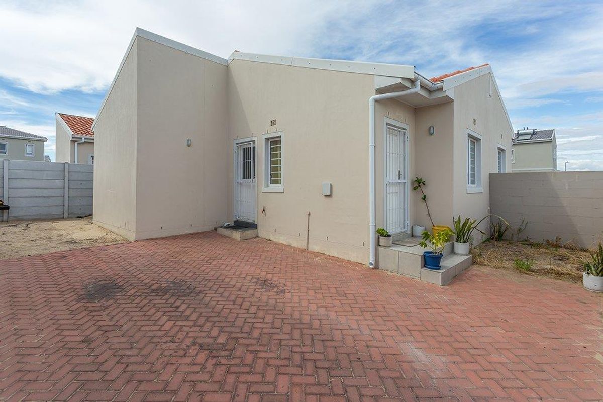Rear exterior view of the house featuring a paved courtyard area, security gates, and perimeter boundary walls.