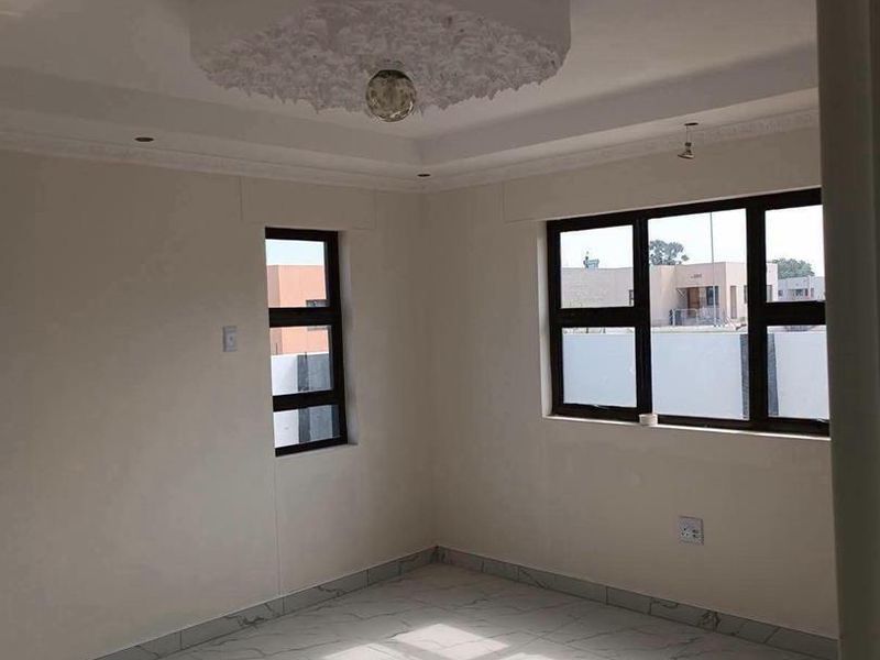 A bright, empty living area featuring modern marble-look tiled flooring, decorative ceiling detailing, and large aluminium-framed windows.