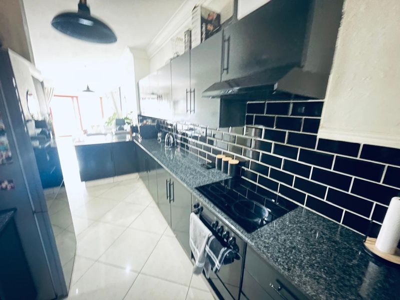 Modern kitchen featuring sleek black cabinetry, contrasting subway tile backsplash, granite countertops, and integrated cooking appliances with polished tiled flooring.