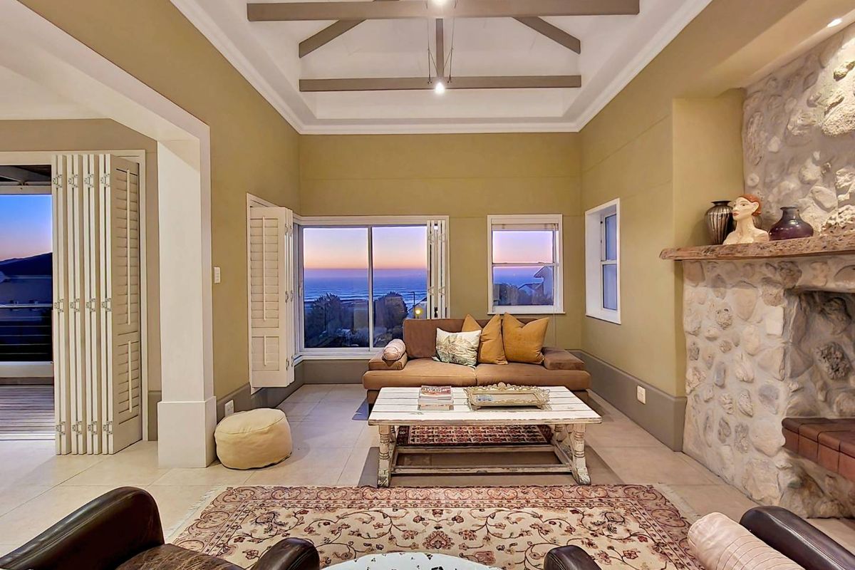 Spacious living room featuring a vaulted ceiling with exposed beams, a prominent stone fireplace, and large windows offering scenic coastal views.