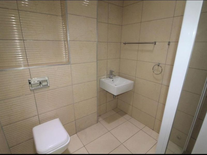 A clean, modern bathroom featuring neutral wall and floor tiles, a wall-mounted toilet, a compact basin, and a shower enclosure.