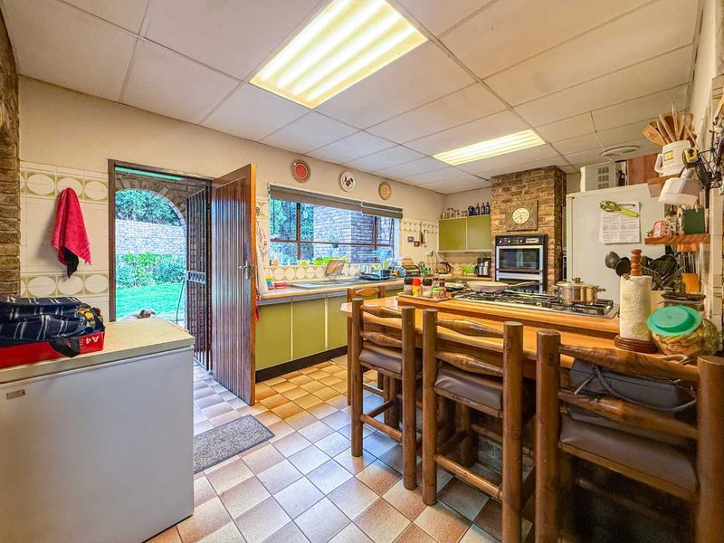 A dated kitchen featuring brick accents, tiled flooring, built-in oven, and direct access to the rear garden area.