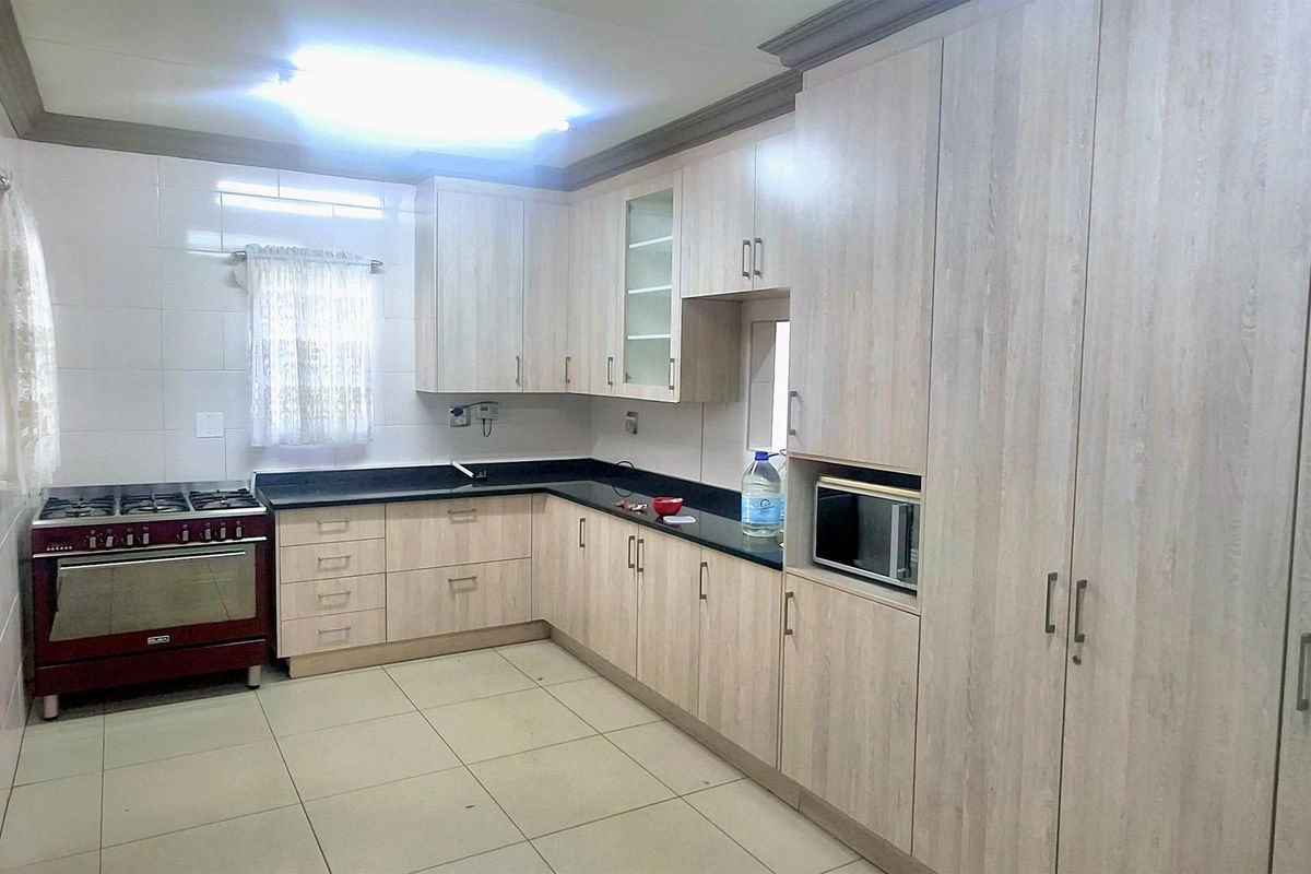 A functional kitchen featuring light wood-grain cabinetry, dark granite countertops, a gas stove, and built-in microwave with neutral tiled flooring and backsplash.