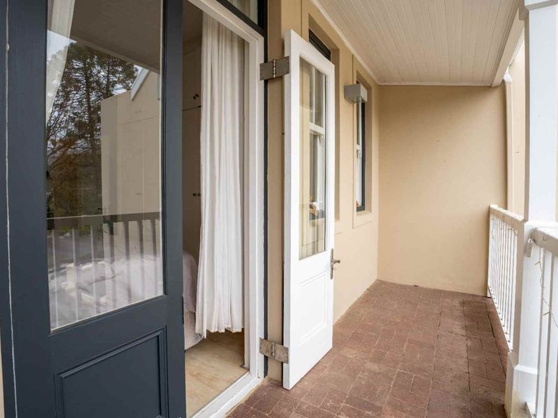 A covered balcony featuring brick paving, a protective railing, and direct access to the interior through glass-paneled doors.