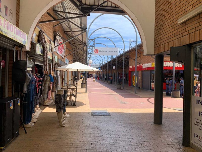 A view of the Bellstar Junction retail walkway featuring brick facades, metal archway structures, and paved pedestrian access between storefronts.