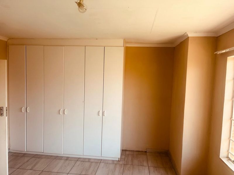 An empty bedroom featuring built-in cupboards, tiled flooring, and a window with security bars, offering a blank canvas for renovation.