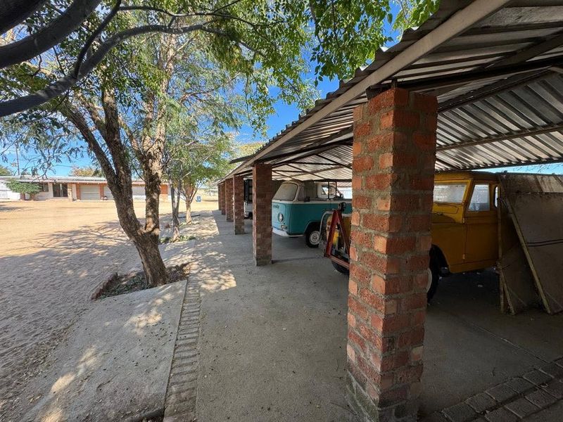 A covered outdoor parking area featuring brick support pillars and a corrugated metal roof, providing sheltered storage space on the property.