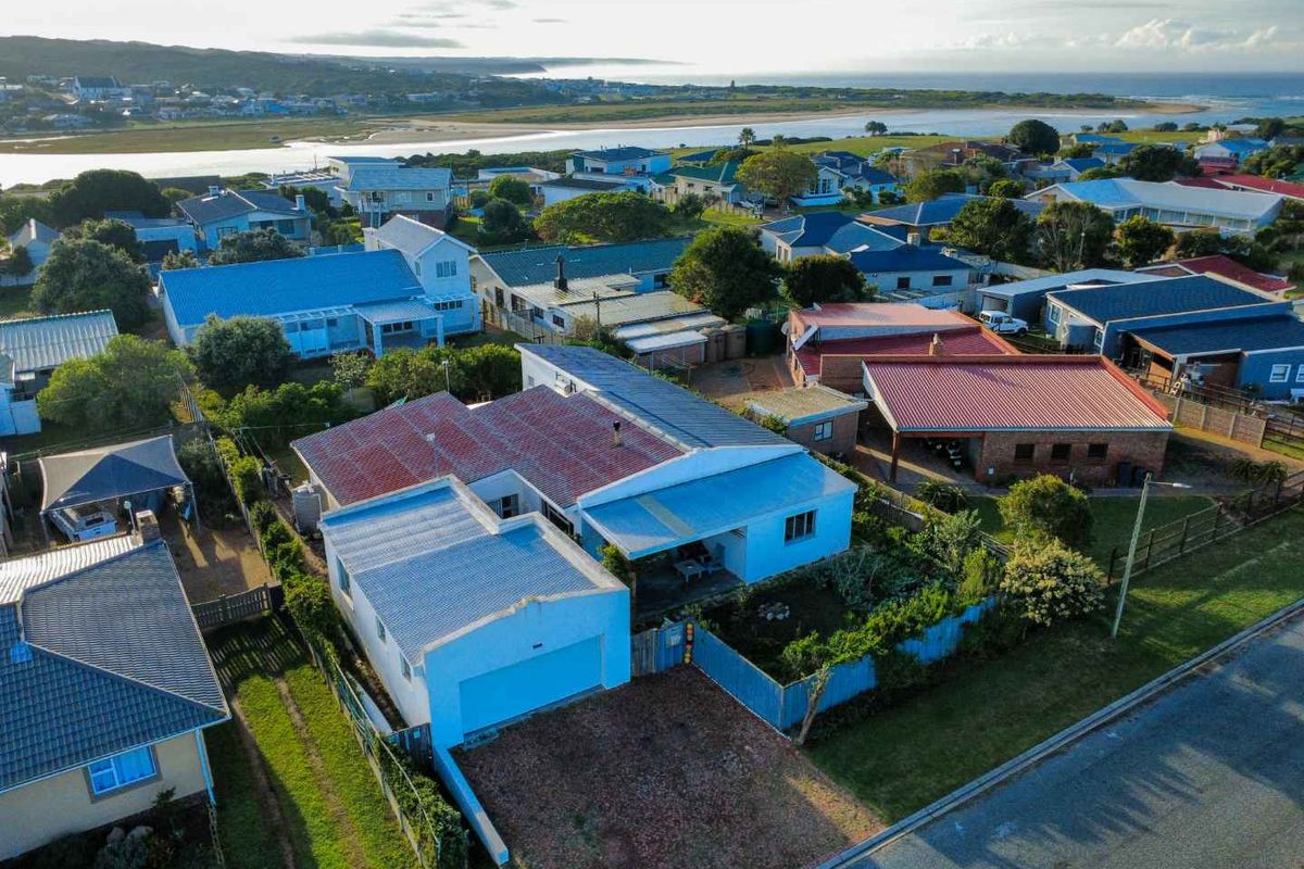 Aerial view of a residential property featuring a corrugated metal roof, single garage, and established garden, situated in a coastal neighborhood.