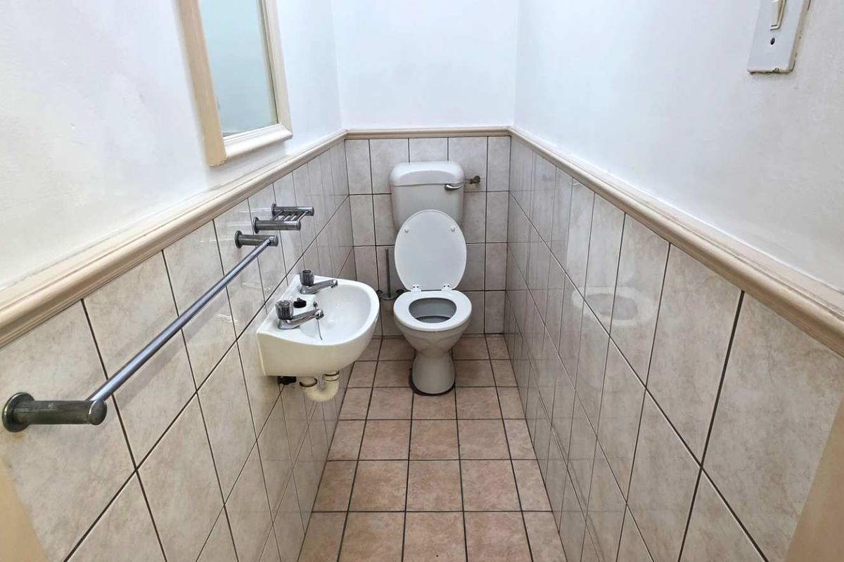 A compact industrial restroom featuring a wall-mounted basin, toilet, and half-height tiled walls with a chrome towel rail.