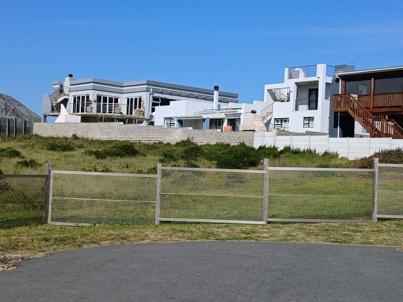 A view of the residential property from the street, featuring a perimeter fence, retaining wall, and paved driveway area.