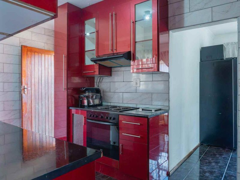 A functional kitchen featuring glossy red cabinetry, built-in oven with hob, extractor fan, and tiled wall finishes.