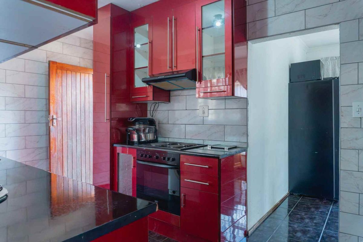 A functional kitchen featuring glossy red cabinetry, built-in oven with hob, extractor fan, and tiled wall finishes.