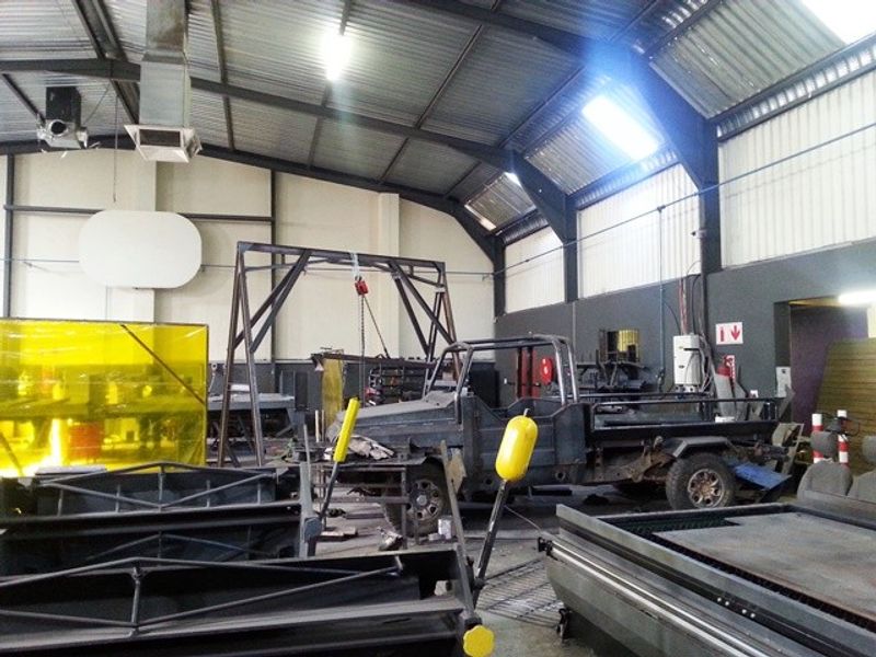Industrial workshop space featuring high ceilings with exposed steel trusses, corrugated metal roofing, and durable concrete flooring suitable for heavy-duty operations.