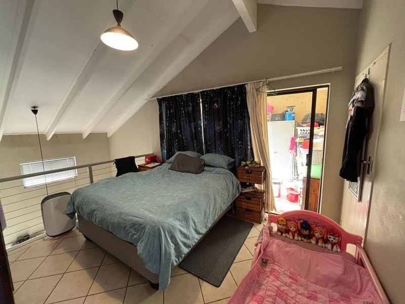 A loft-style bedroom featuring vaulted ceilings with exposed rafters, tiled flooring, and a metal balustrade overlooking the lower level.