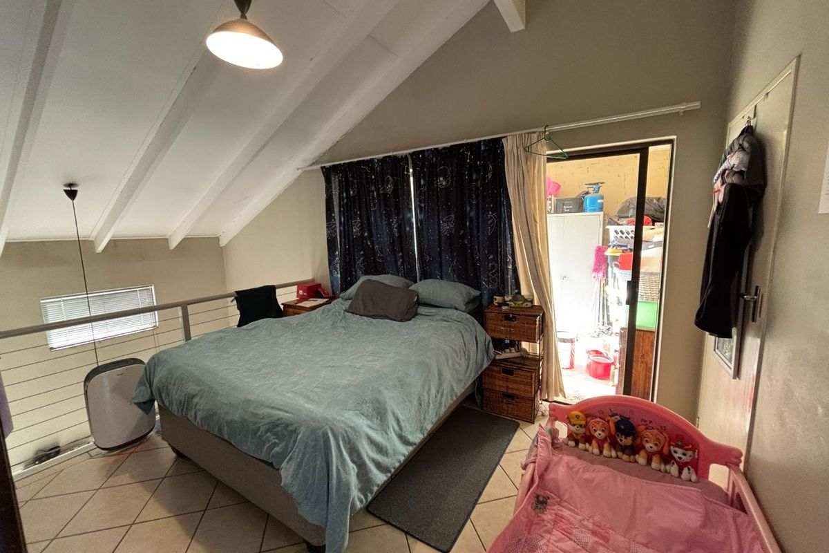 A loft-style bedroom featuring vaulted ceilings with exposed rafters, tiled flooring, and a metal balustrade overlooking the lower level.