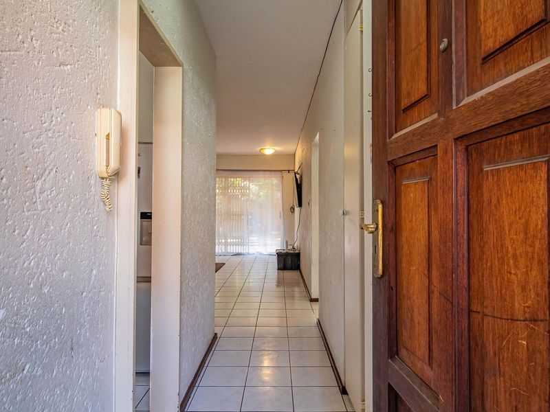 A functional apartment entrance hallway featuring tiled flooring, a solid wood front door, and an integrated intercom system leading into the main living area.